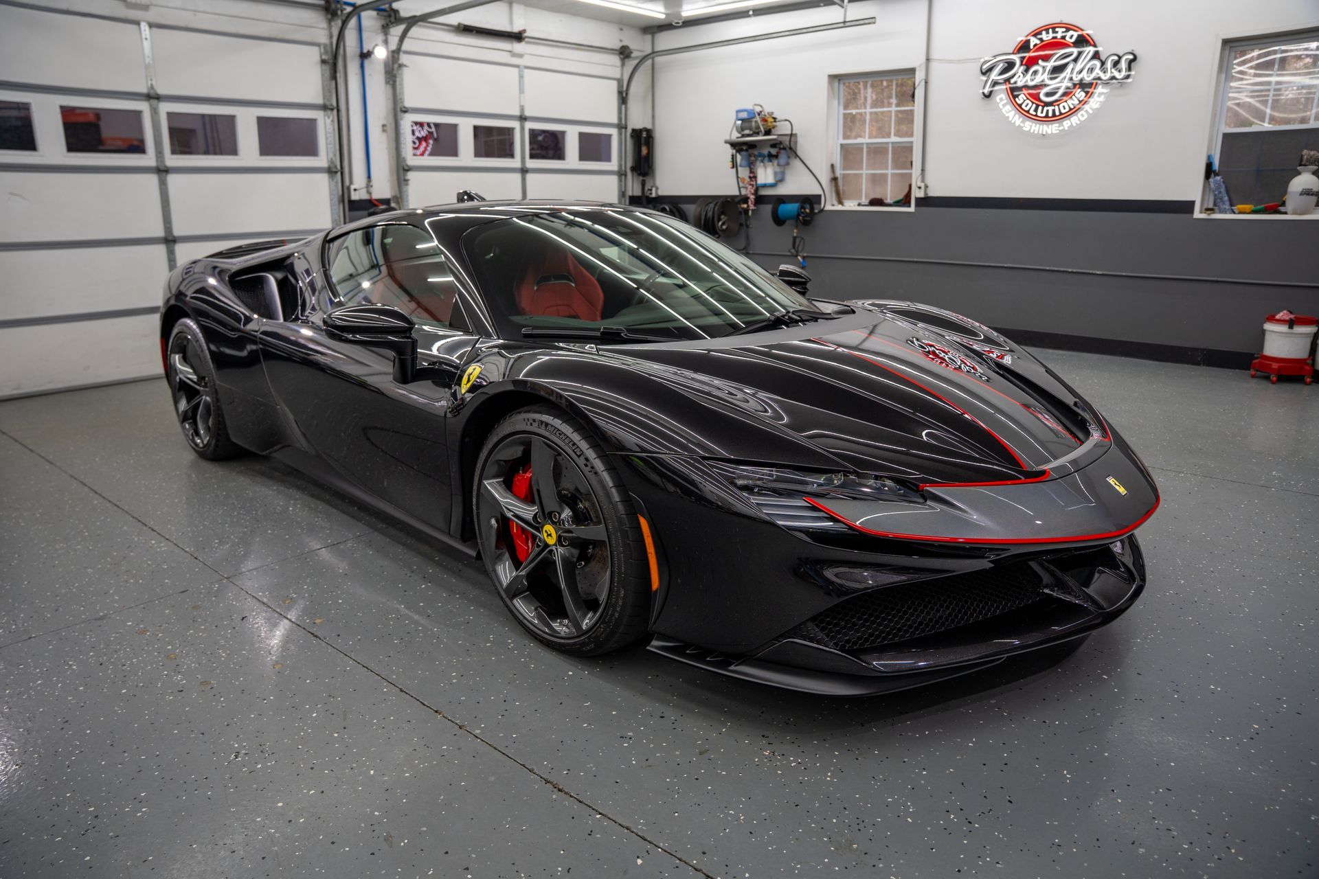 Black Ferrari SF90 Spider convertible in a car garage. Red brake calipers and interior accents.