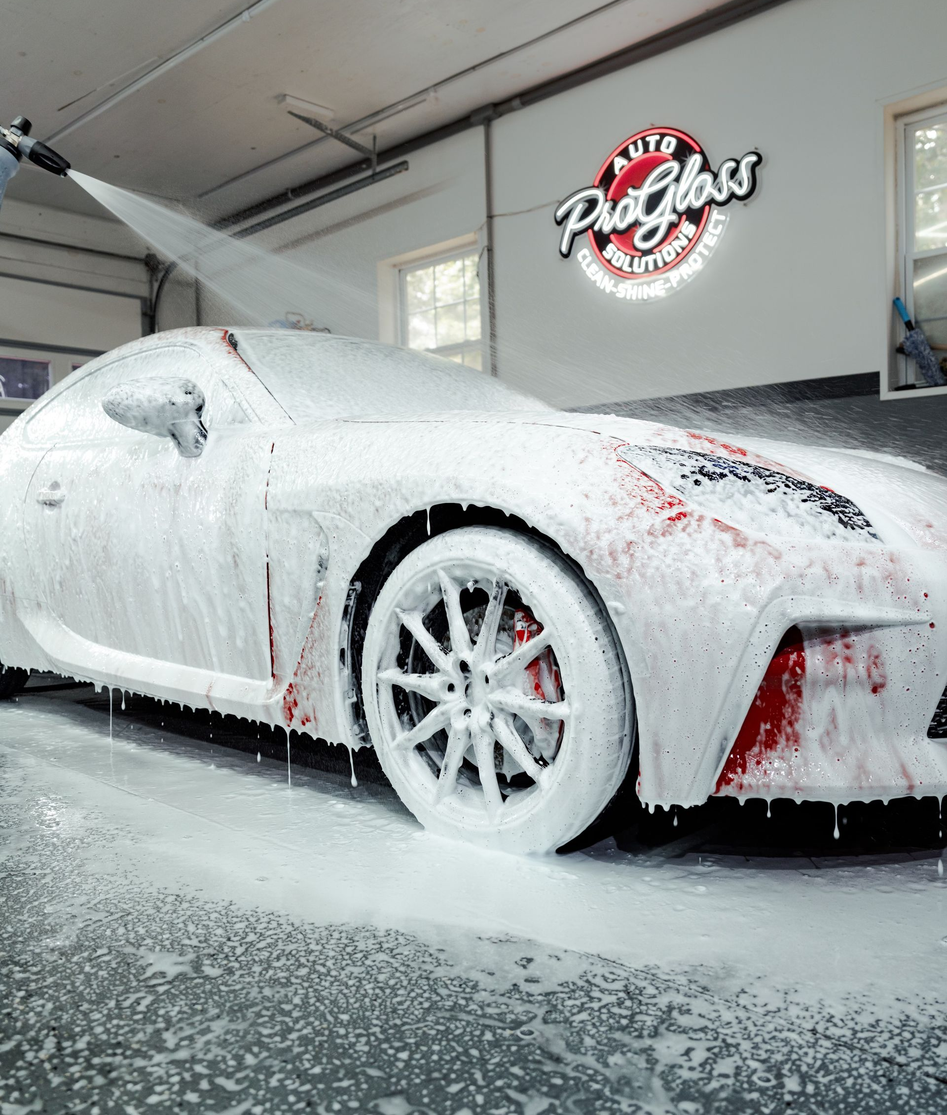 White sports car covered in foam at a car wash, red accents visible.