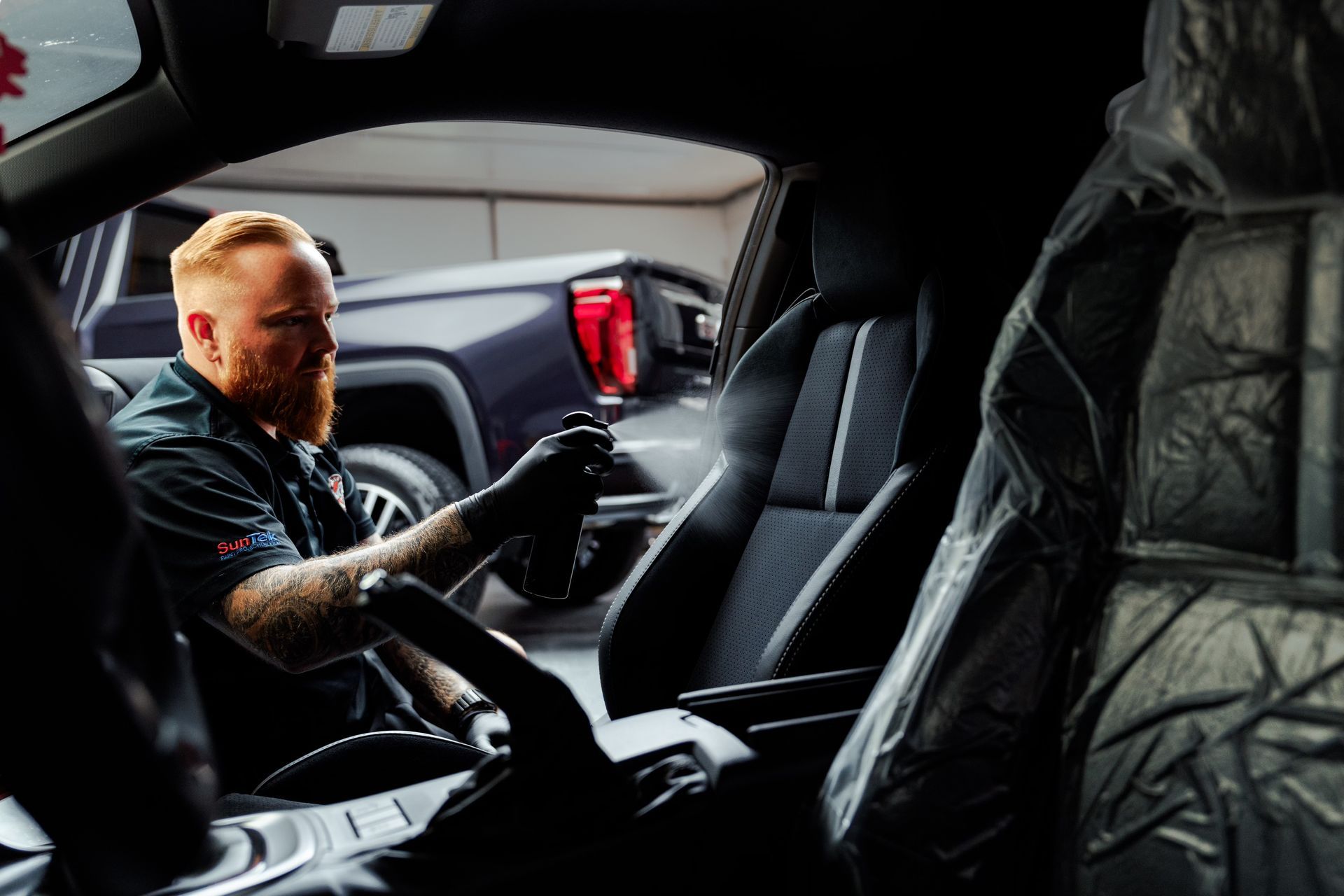 Person cleaning a red car dashboard with blue gloves and a spray bottle.