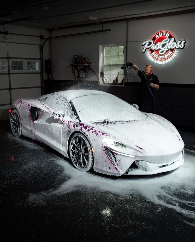 A man washing a white sports car with foam in a garage.
