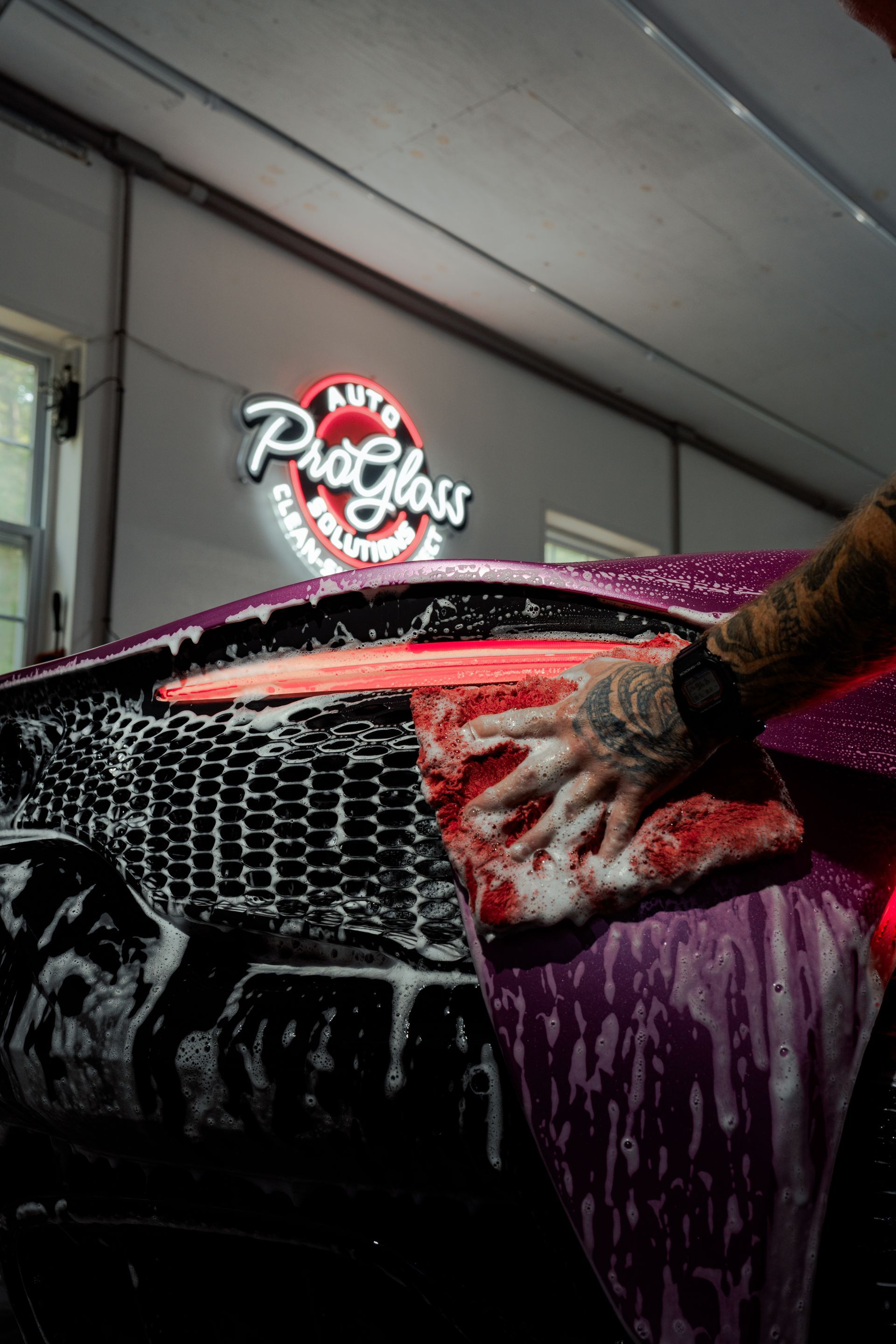 A person washes a purple car with a soapy sponge in a car wash. 