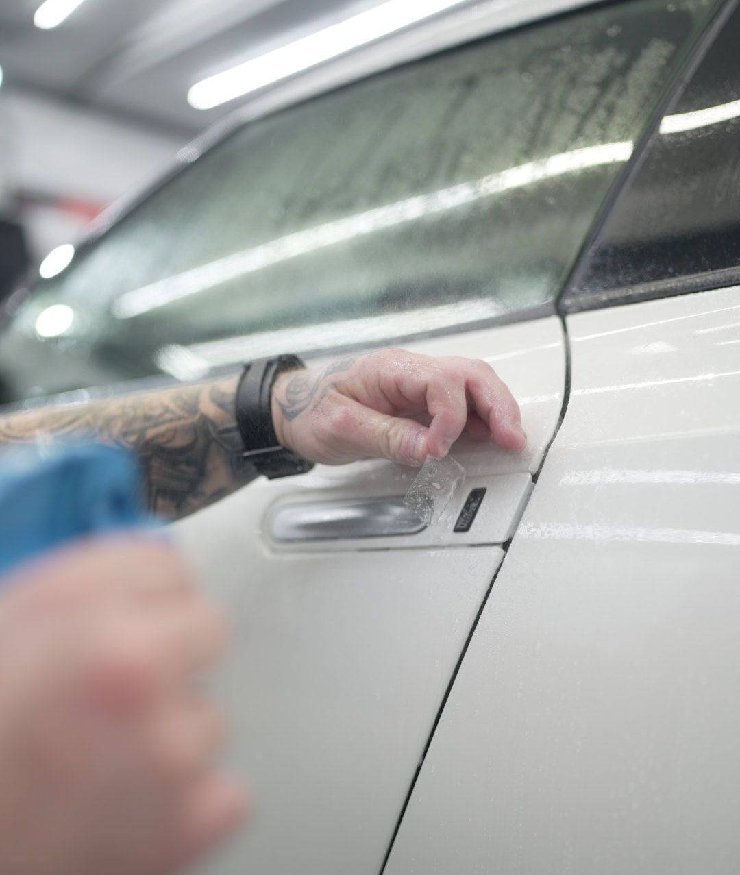 Person applying protective film on a white car door handle in a garage.