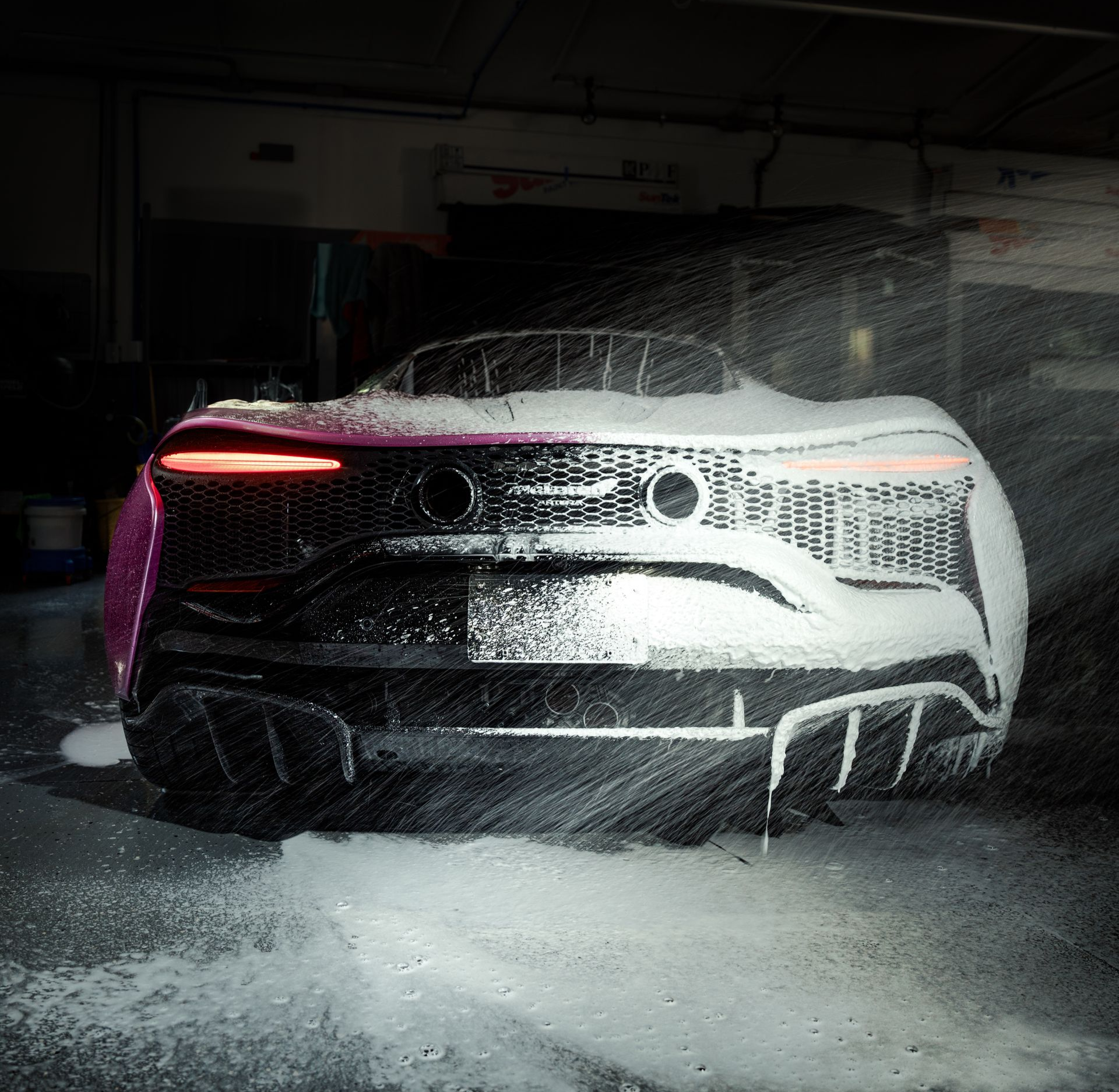 Man applying film to pink car in a garage. He kneels, sprays, and smooths the film.
