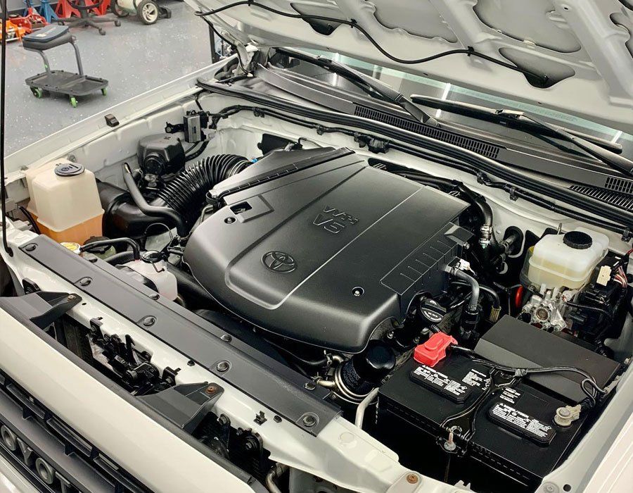 Toyota Tacoma truck engine compartment, black engine cover, white truck body, and tools in a garage.