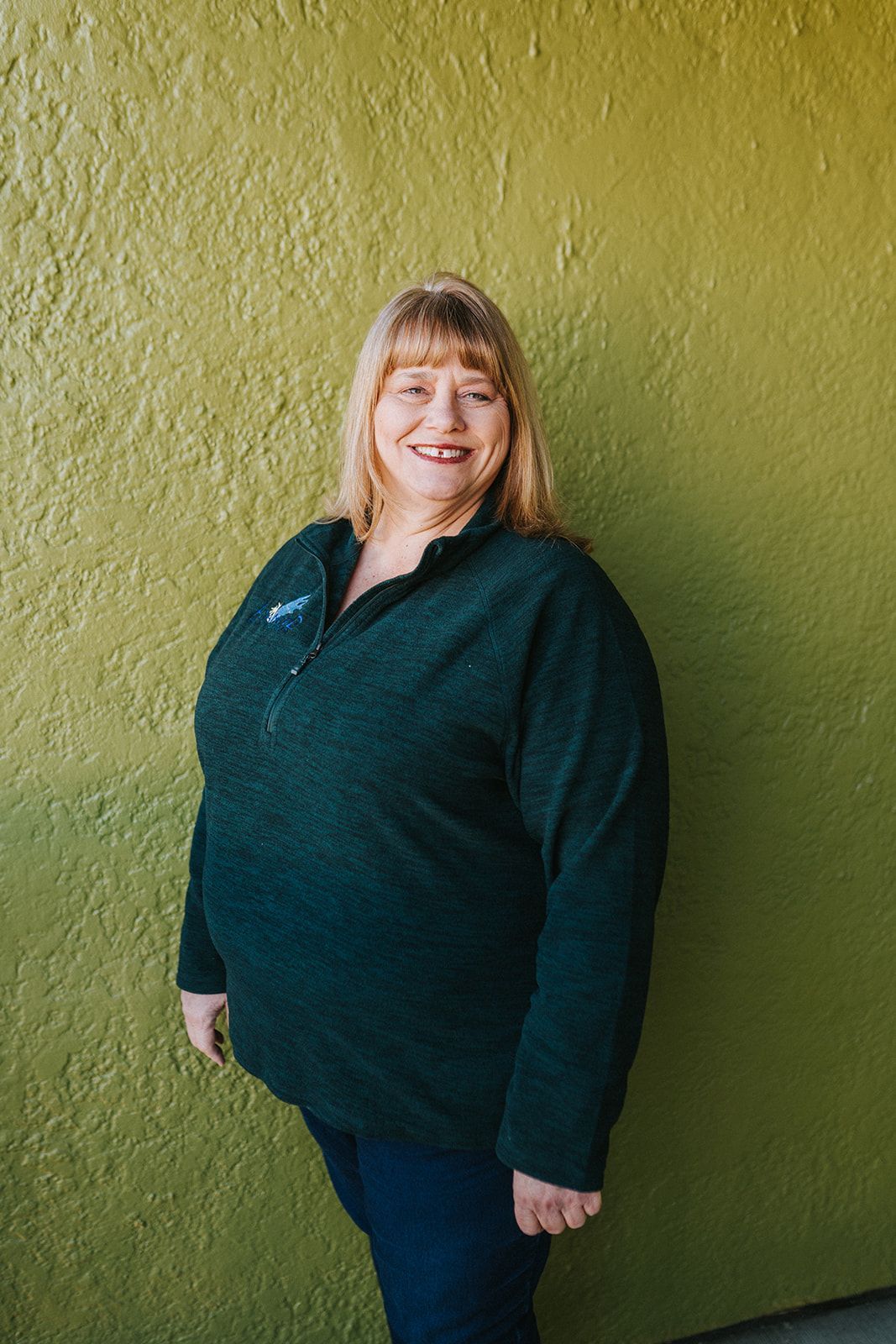 A woman in a green sweater is standing in front of a green wall.