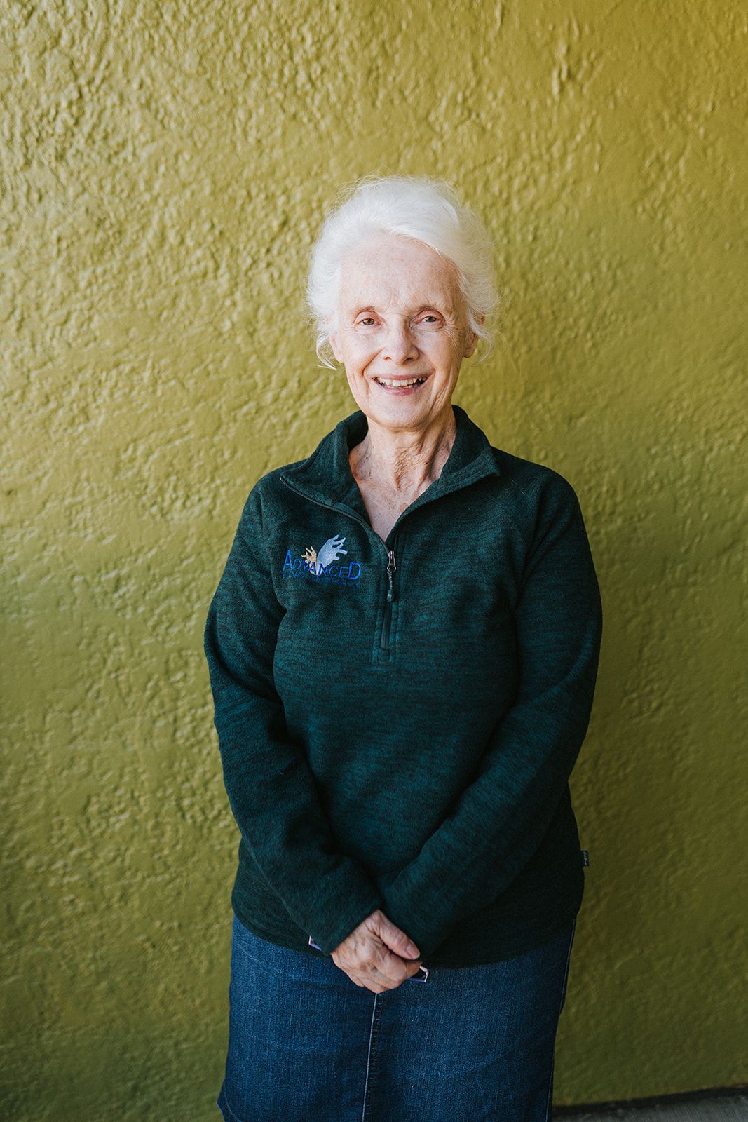 A woman in a green sweater is standing in front of a green wall.