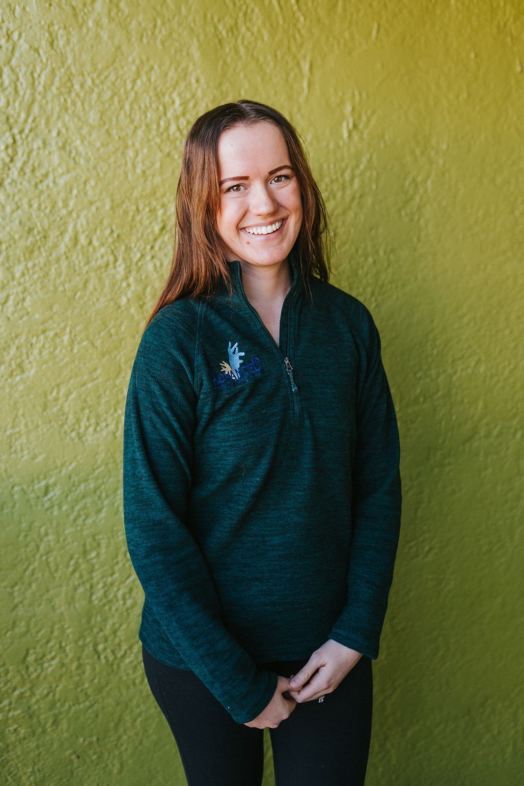 A woman in a green sweater is standing in front of a green wall.
