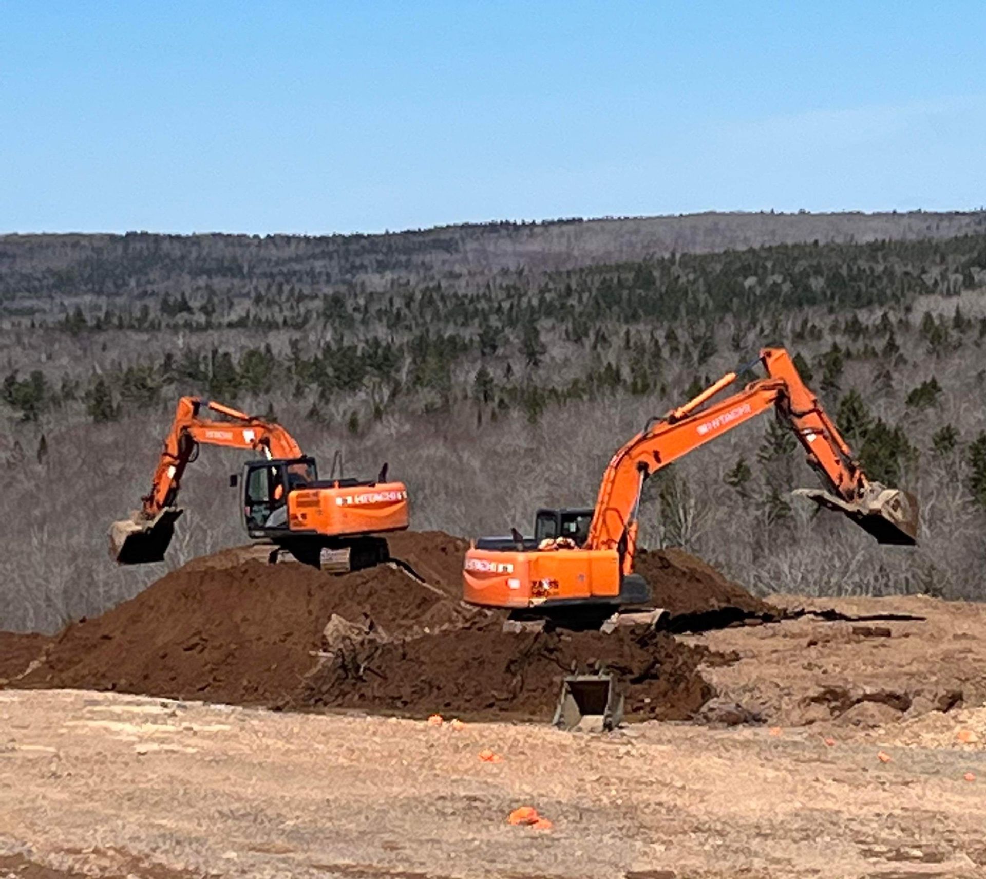 Two orange excavators are working on a dirt field