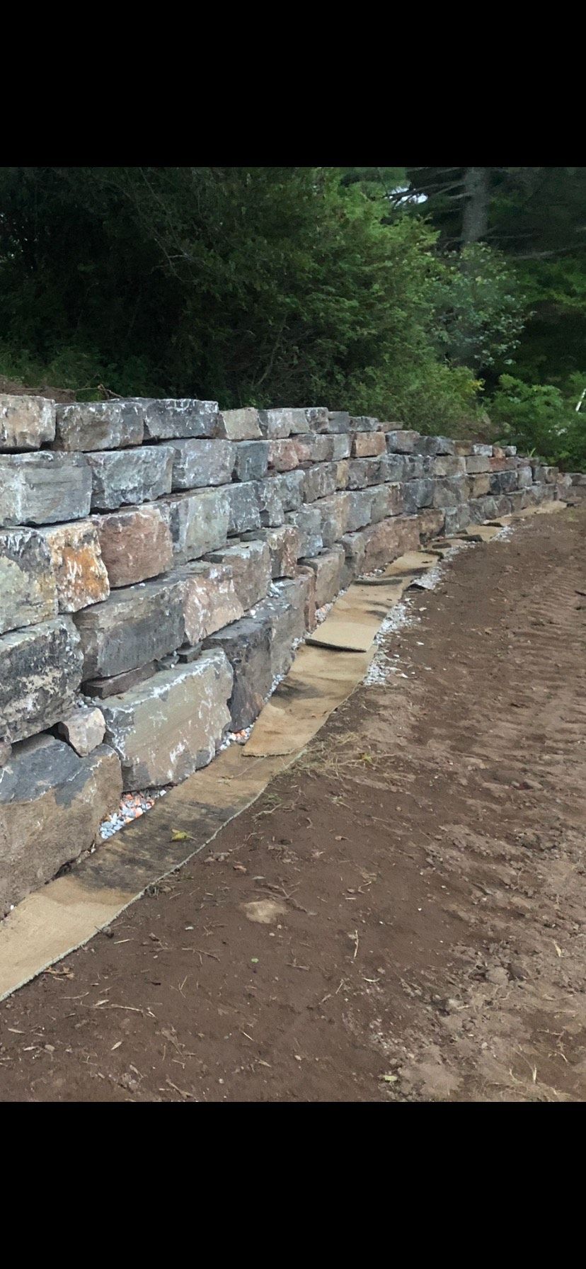 A stone wall is being built next to a dirt road.