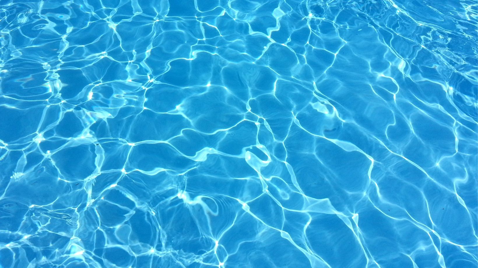 Sunlit blue swimming pool water with shimmering ripples and reflections