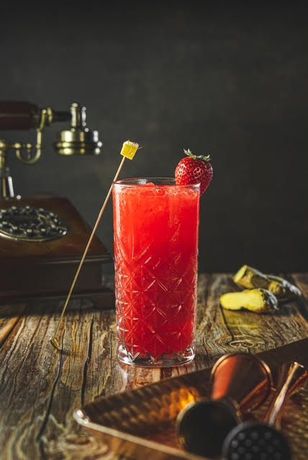 Cóctel rojo en vaso alto con adorno de fresa; mesa rústica de madera, teléfono antiguo.