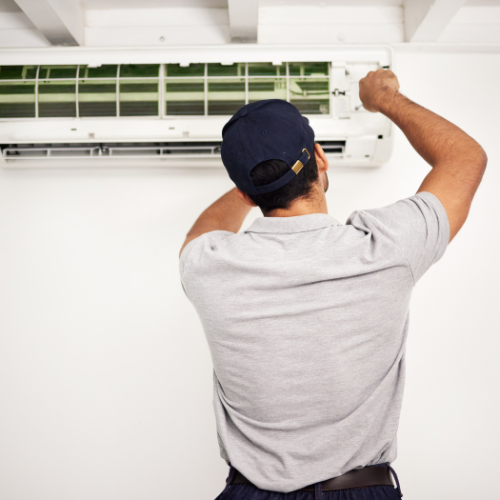 Man in cap fixing wall-mounted air conditioner.