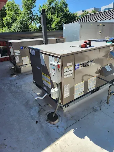 HVAC technicians in blue workwear inspect HVAC units in a large facility.