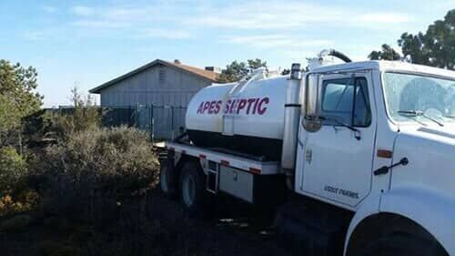 A white septic truck is parked in front of a house.