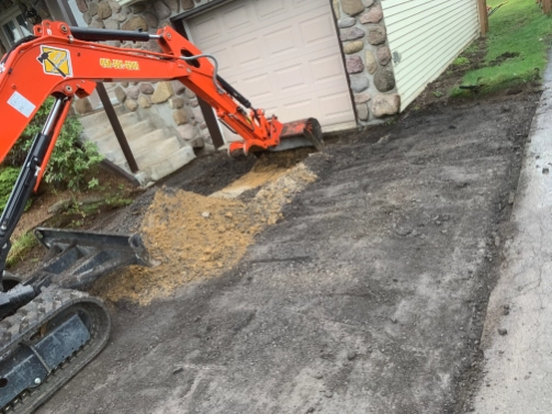 Une petite pelle orange creuse un trou dans le sol devant un garage.