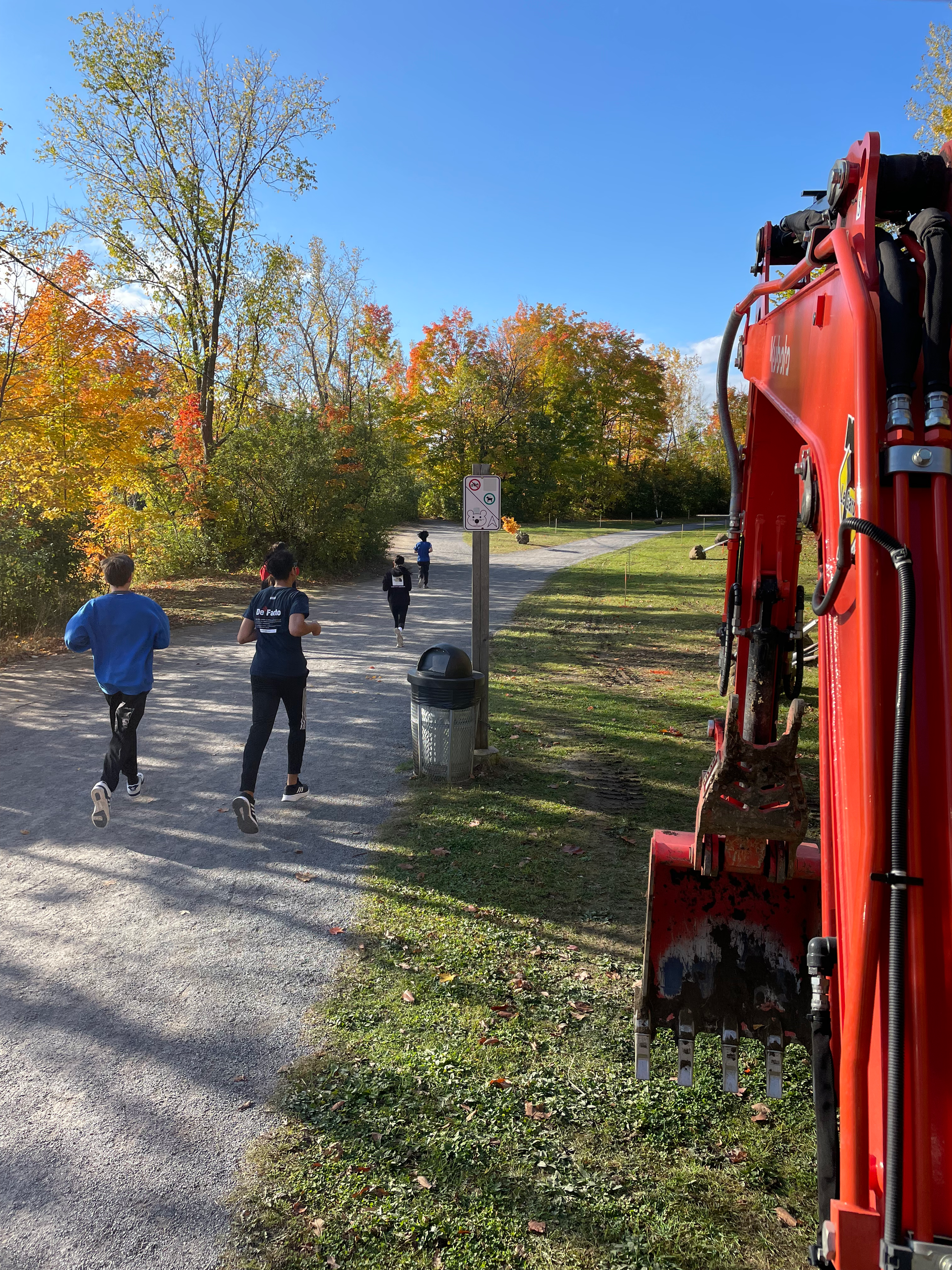 Quelques personnes marchent sur un chemin à côté d'une excavatrice rouge.