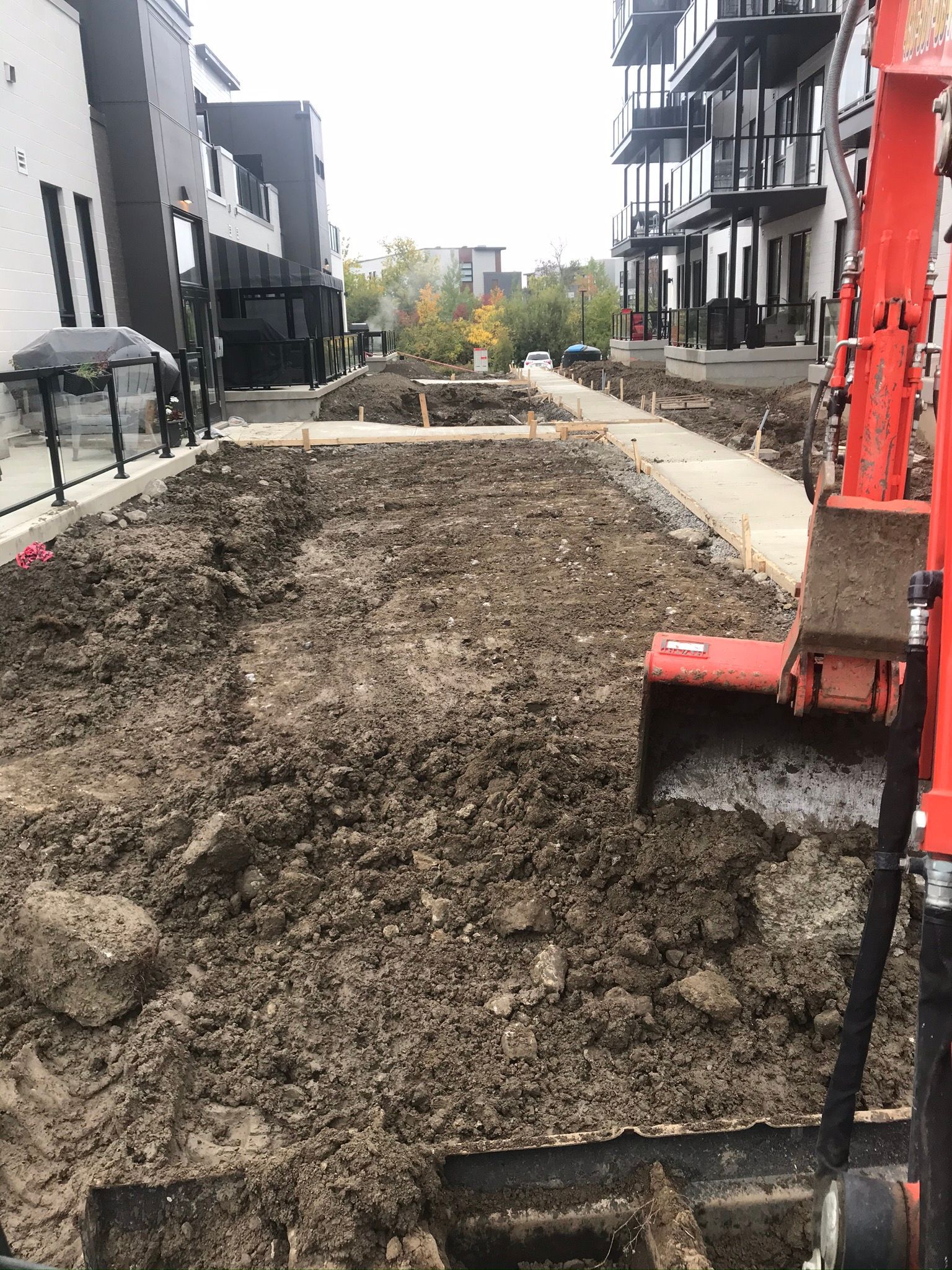 Une excavatrice rouge creuse un trou dans la terre devant un bâtiment.