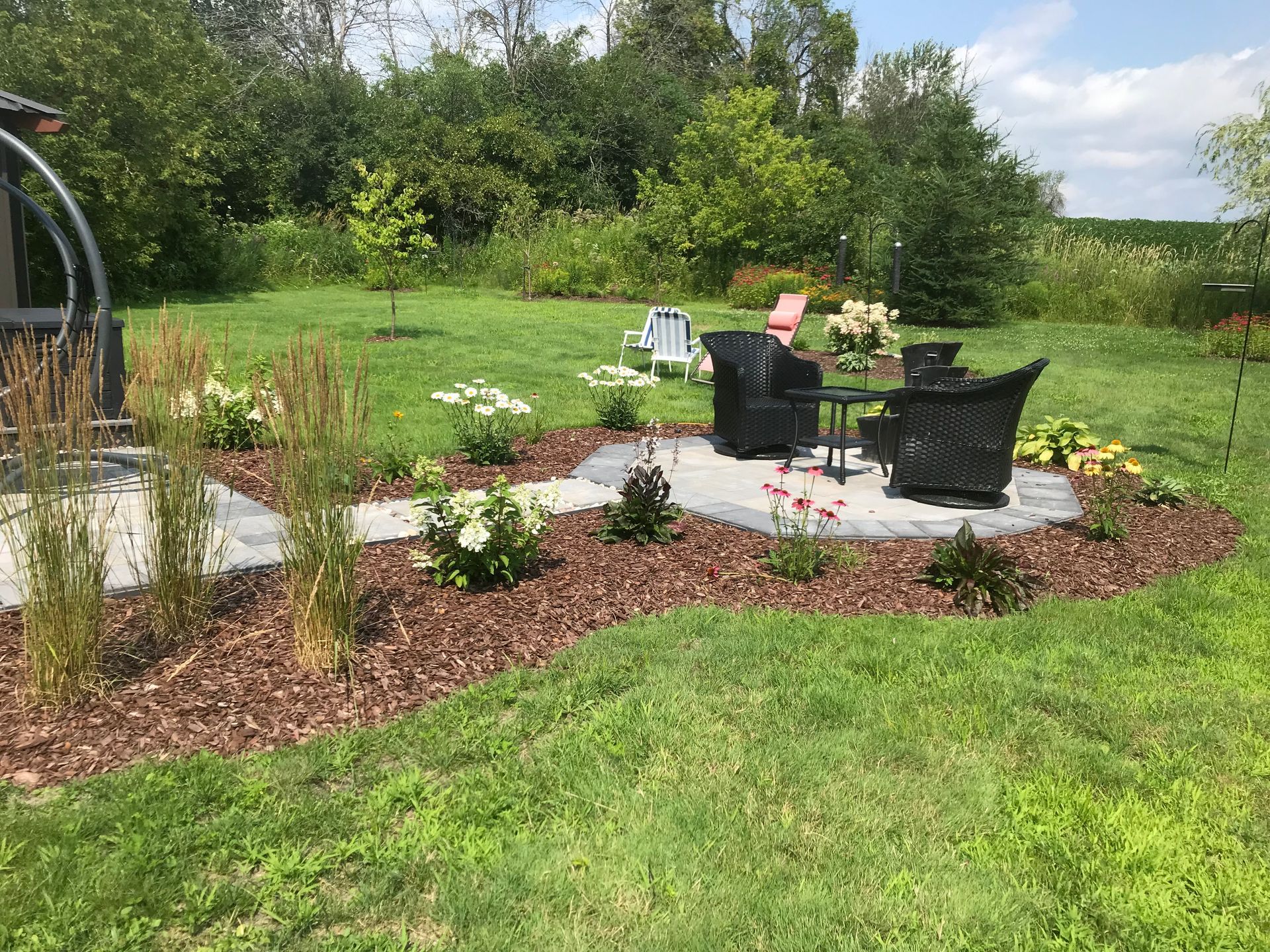 Un patio avec des chaises et une table au milieu d'un champ verdoyant.