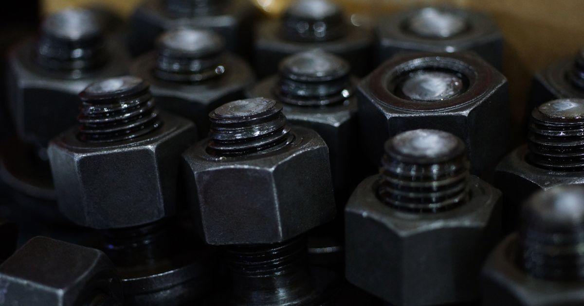 Close-up of stacked black metal nuts and bolts on a dark surface