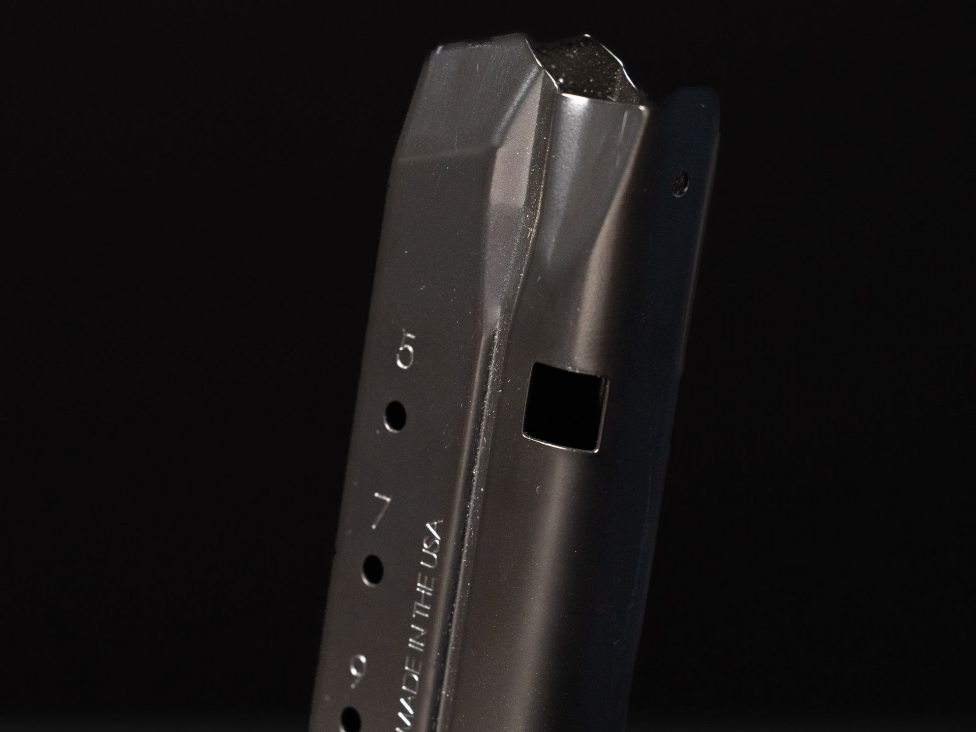 Black gun magazine with visible bullet count holes, angled against a dark background.