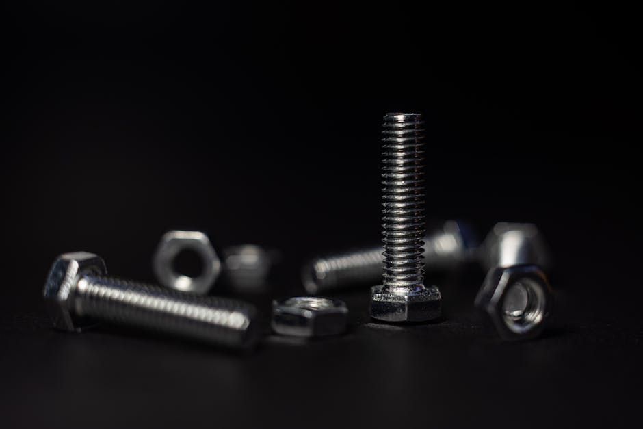 Several silver metal bolts and nuts scattered on a dark surface