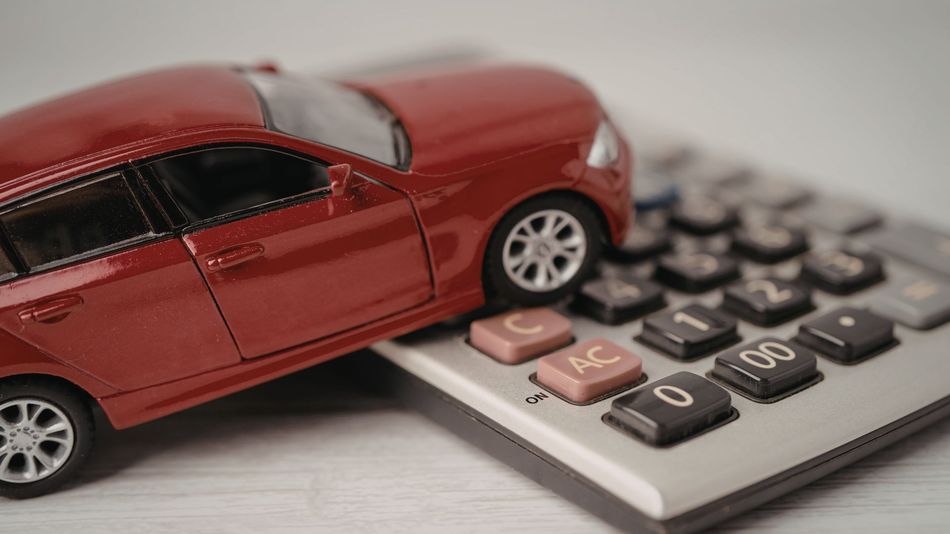 Red toy car parked on a calculator, symbolizing car costs or finance.