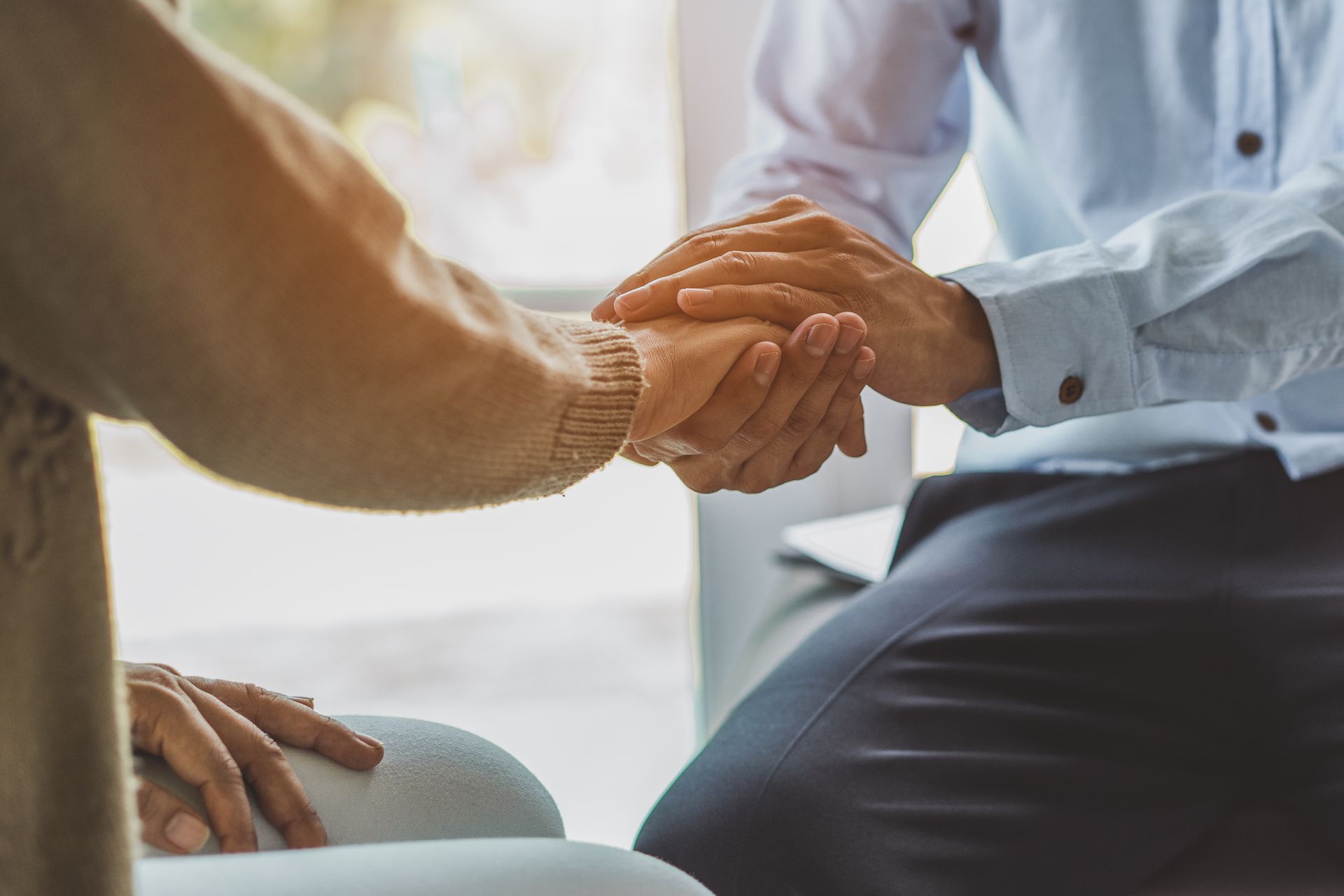 Person comforting another, holding their hands in a supportive gesture.