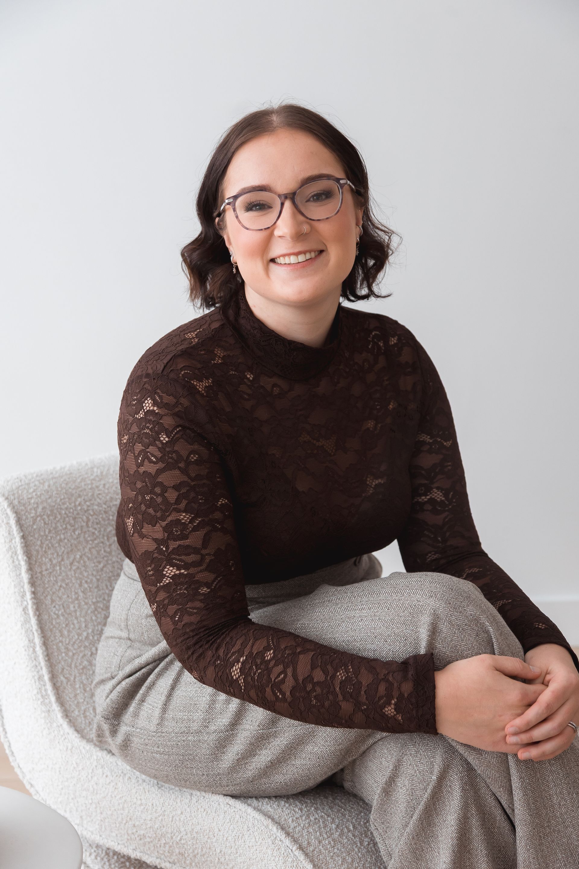 Woman in a Brown Tops  smiles while seated in a gray armchair.