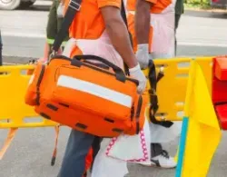 Emergency medical personnel with an orange medical bag and stretcher.
