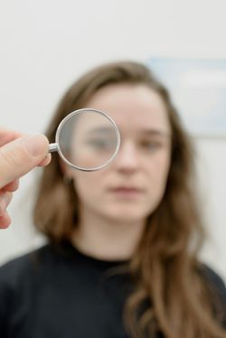 Person receiving eye exam, hand holding lens in front of face, indoors, blurred background.