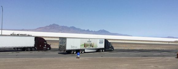 Two semi trucks are parked in a parking lot with mountains in the background.