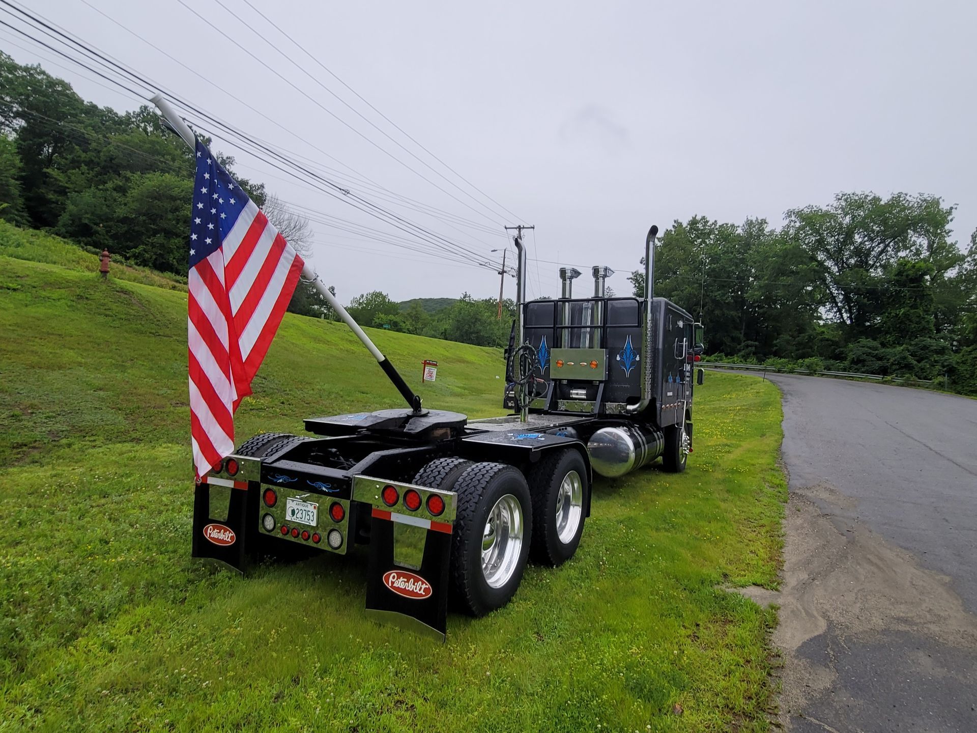 A semi truck with an american flag on the back is parked on the side of the road.