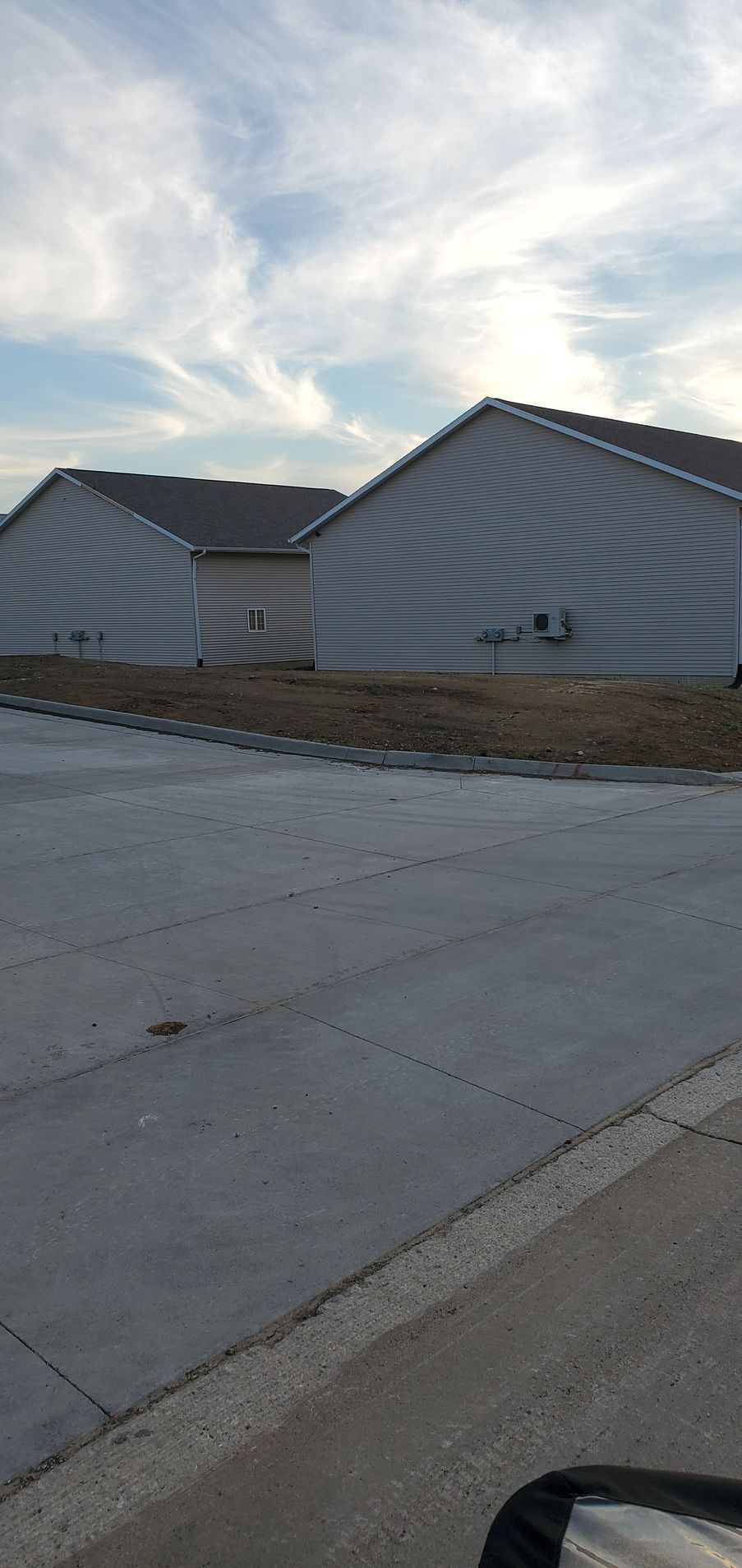 Buildings with corrugated siding along a gray paved road, under a cloudy sky.