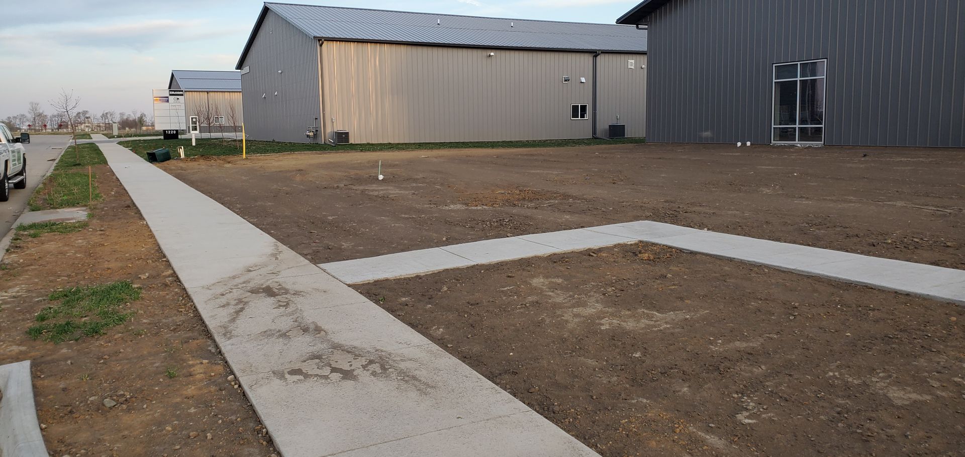 A concrete sidewalk leads past dirt and metal buildings.