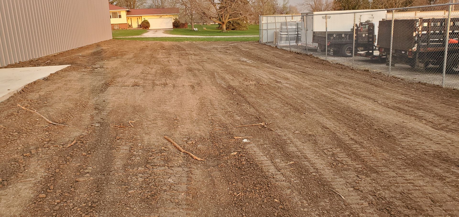 Brown dirt lot next to a building and fenced area.