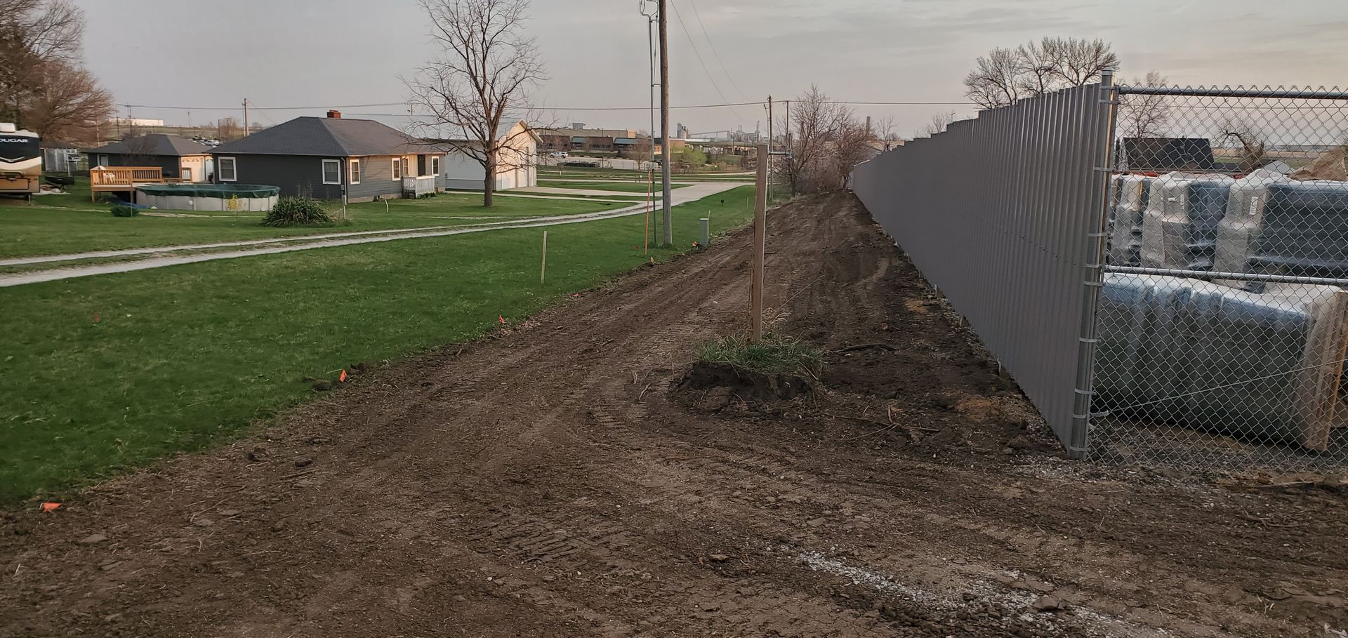 A dirt embankment with a chain link fence, houses in the background, gray material on the right.