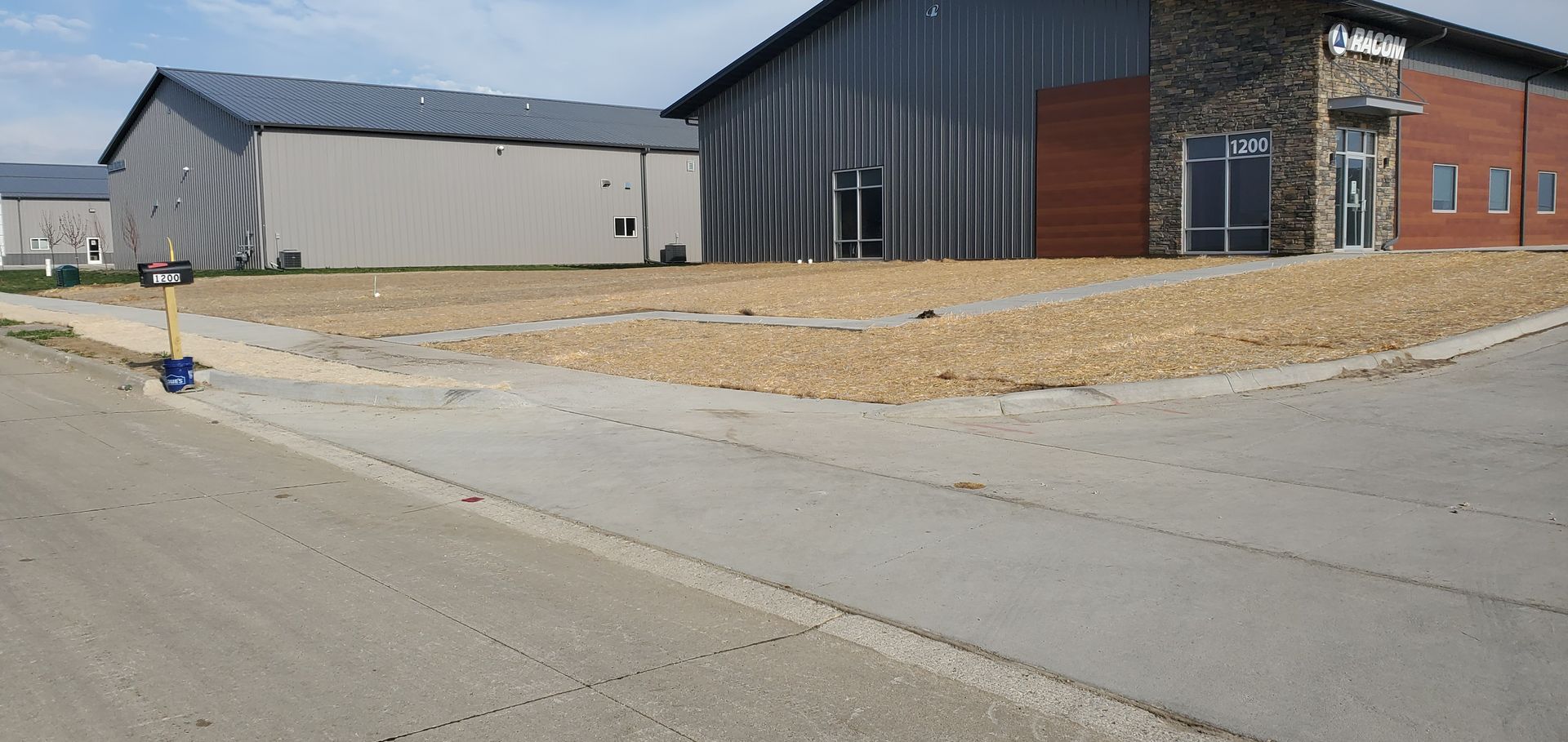Buildings and gravel area. Concrete road in the foreground. Blue sky.