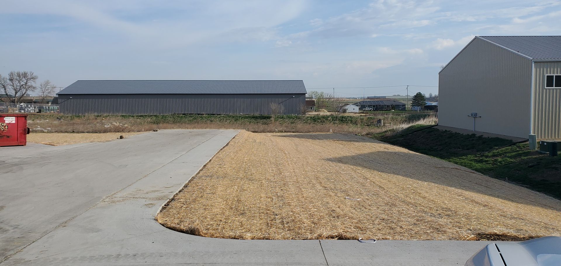 Exterior of industrial buildings on a partly cloudy day. A gravel area is in the foreground.