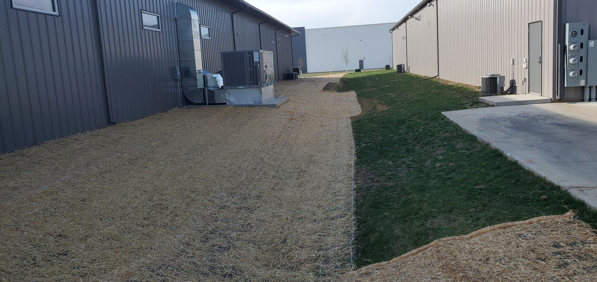 A gravel and grass area between two industrial buildings.