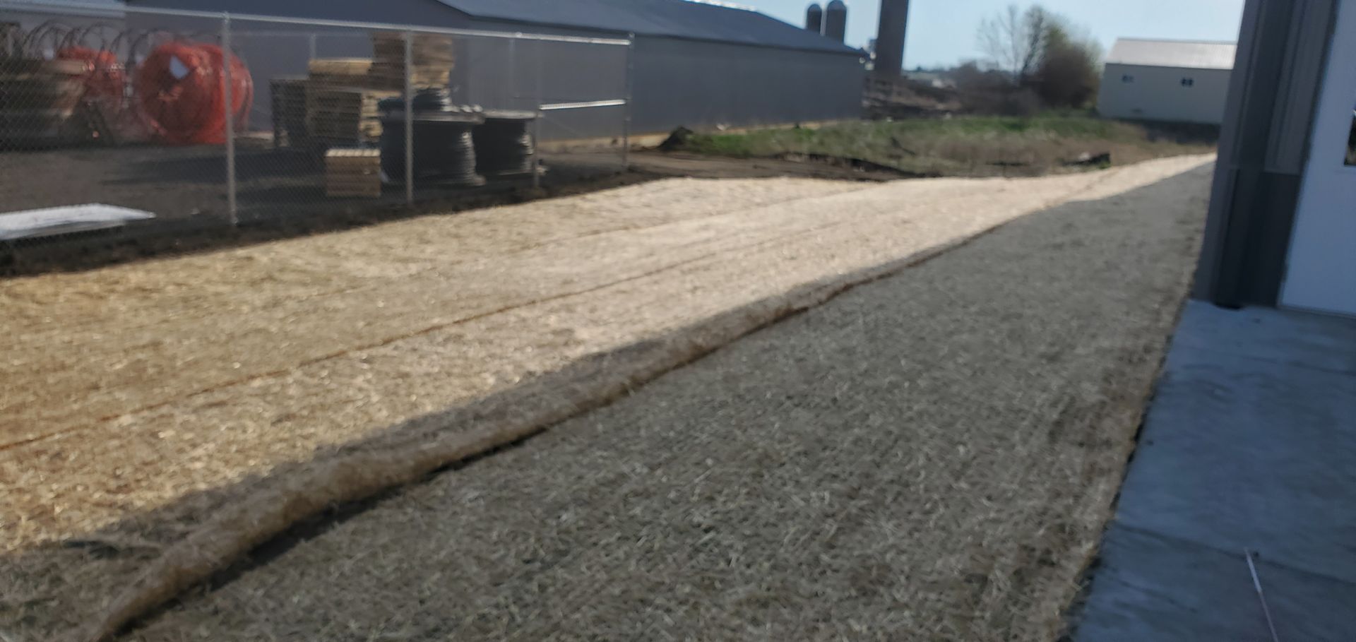 A gravel driveway next to a section covered in straw, next to a building.
