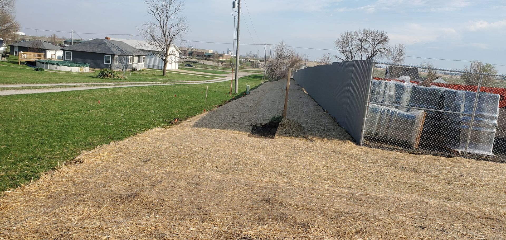 View of a grass and mulch landscape with buildings and a corrugated metal structure.