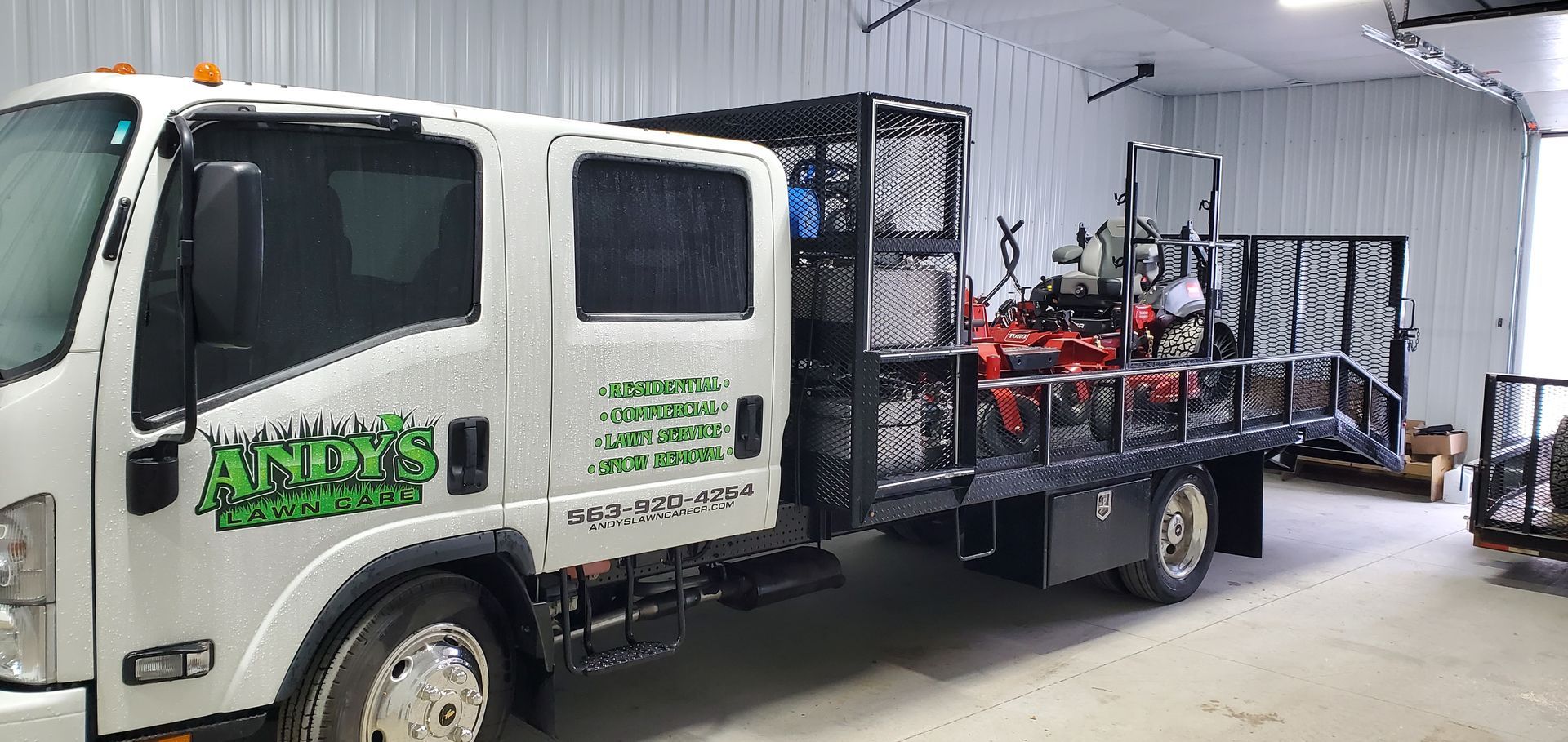 White landscape truck parked in a garage with landscaping equipment on its bed.
