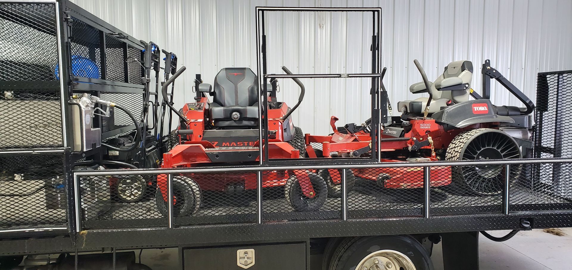 Truck bed with two red lawn mowers, tools, and a storage container.
