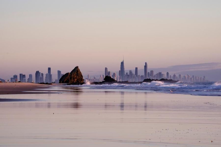 A Beach with A City Skyline in The Background and A Rock in The Foreground — Dent Motive in Broadbeach, QLD