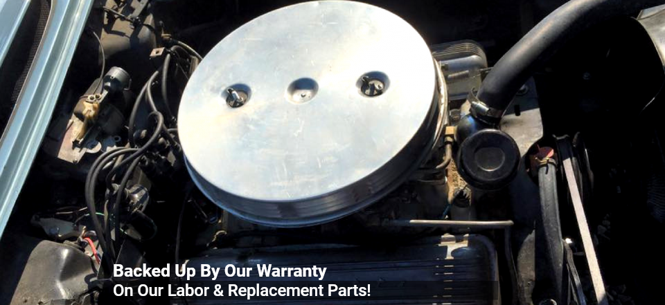 A top-down view of a classic car engine featuring a large, round, polished metal air cleaner cover.