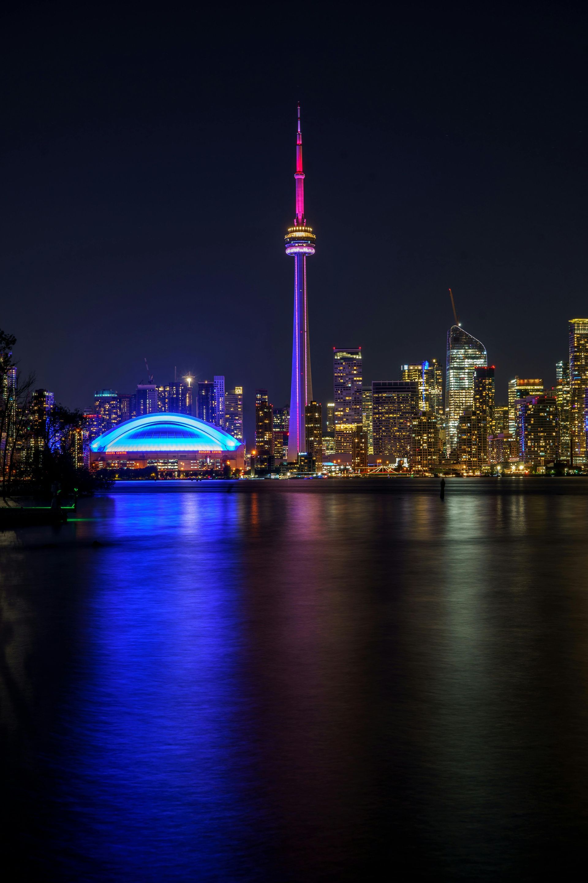Toronto skyline at night, with CN Tower and illuminated buildings reflected in the water.