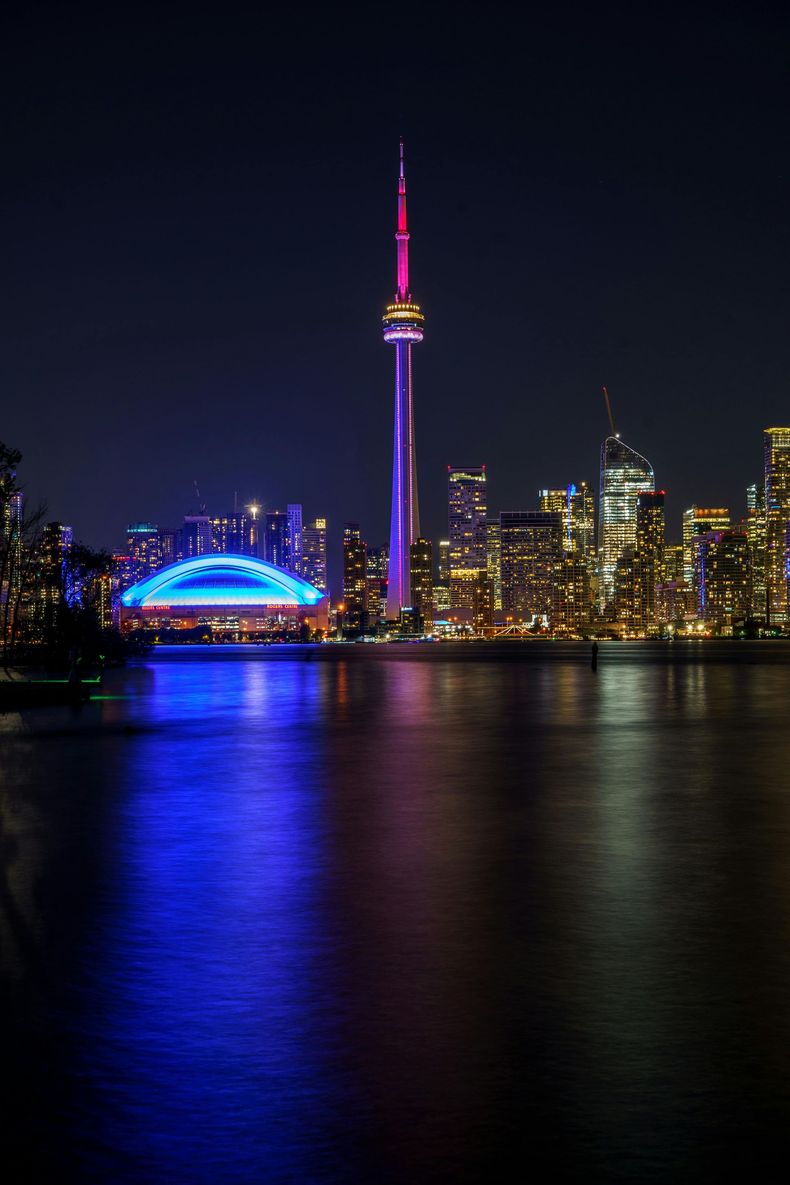 Toronto skyline at night, with CN Tower and illuminated buildings reflected in the water.