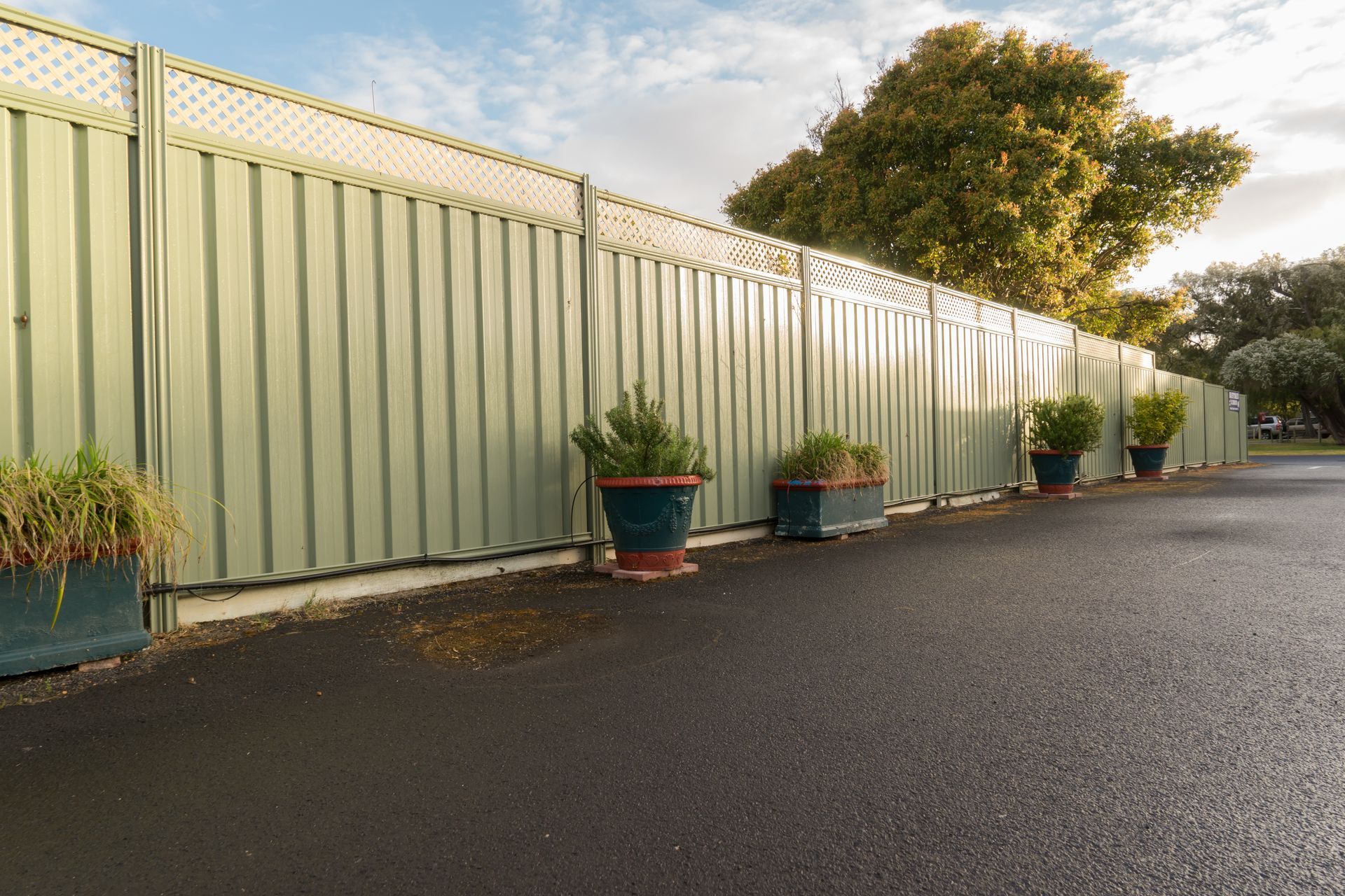 A row of potted plants sitting next to a green fence.