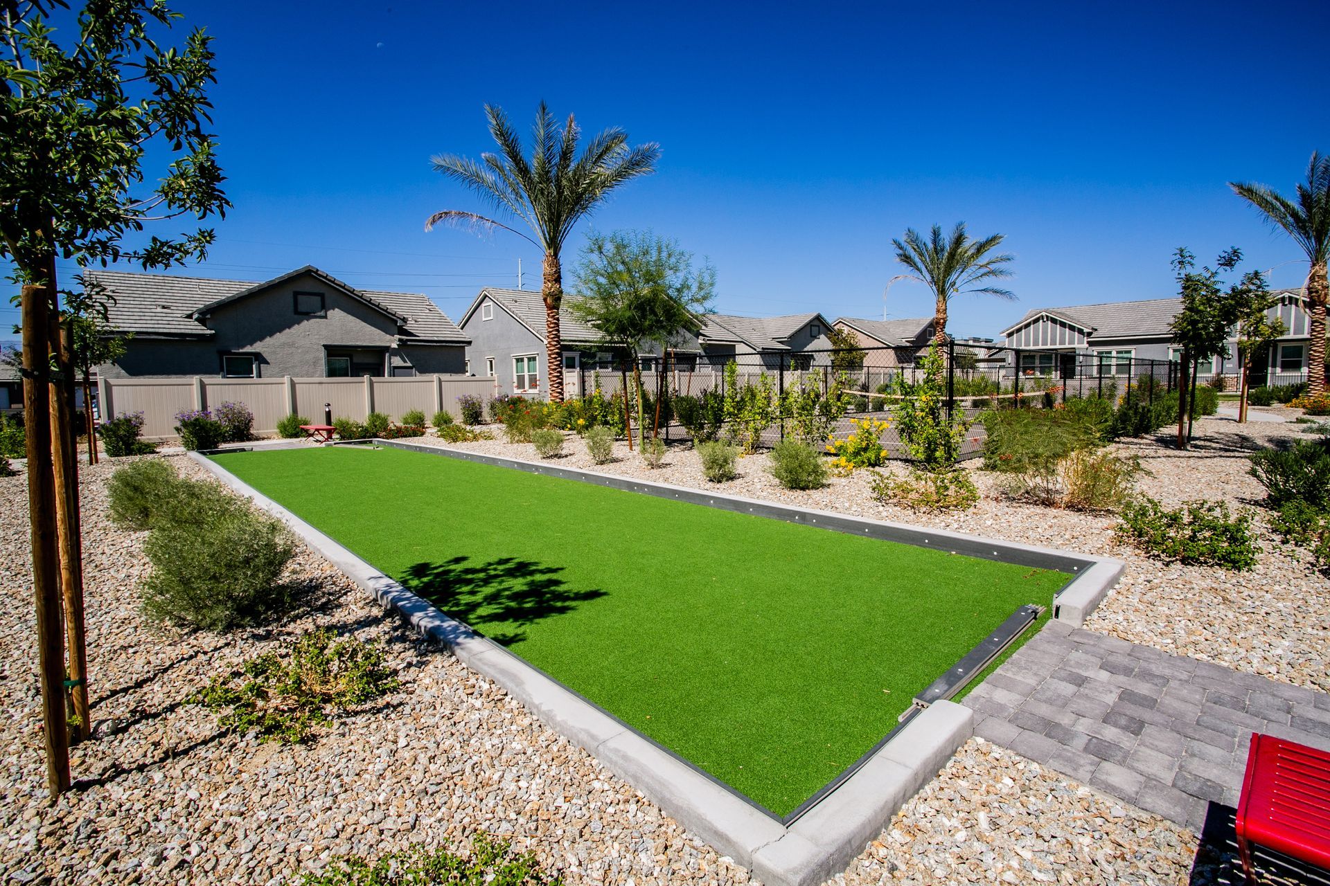 A bowling alley in a backyard with palm trees and houses in the background.