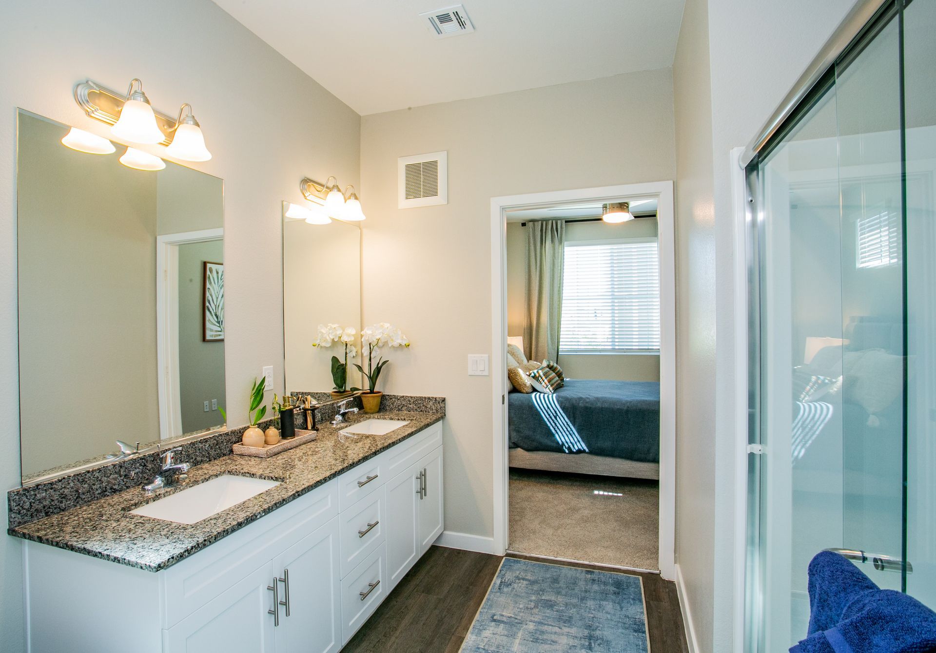 A bathroom with two sinks and a walk in shower leading to a bedroom.
